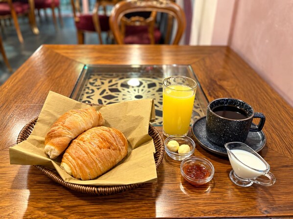 Un desayuno con croissants, zumo de naranja, café y salsas sobre una mesa de madera.