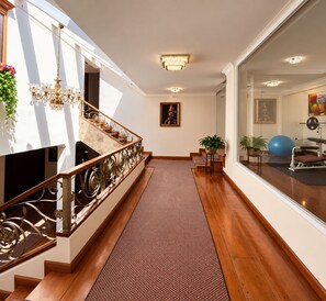 A staircase with a patterned carpet, a chandelier, and a view of a gym area through a glass door. - Dakani Hotel Boutique  (Quito)