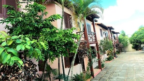 A narrow, paved pathway flanked by lush greenery and traditional-style buildings with wooden balconies. - Branca Tropical Brasil Residencial (Porto Seguro)