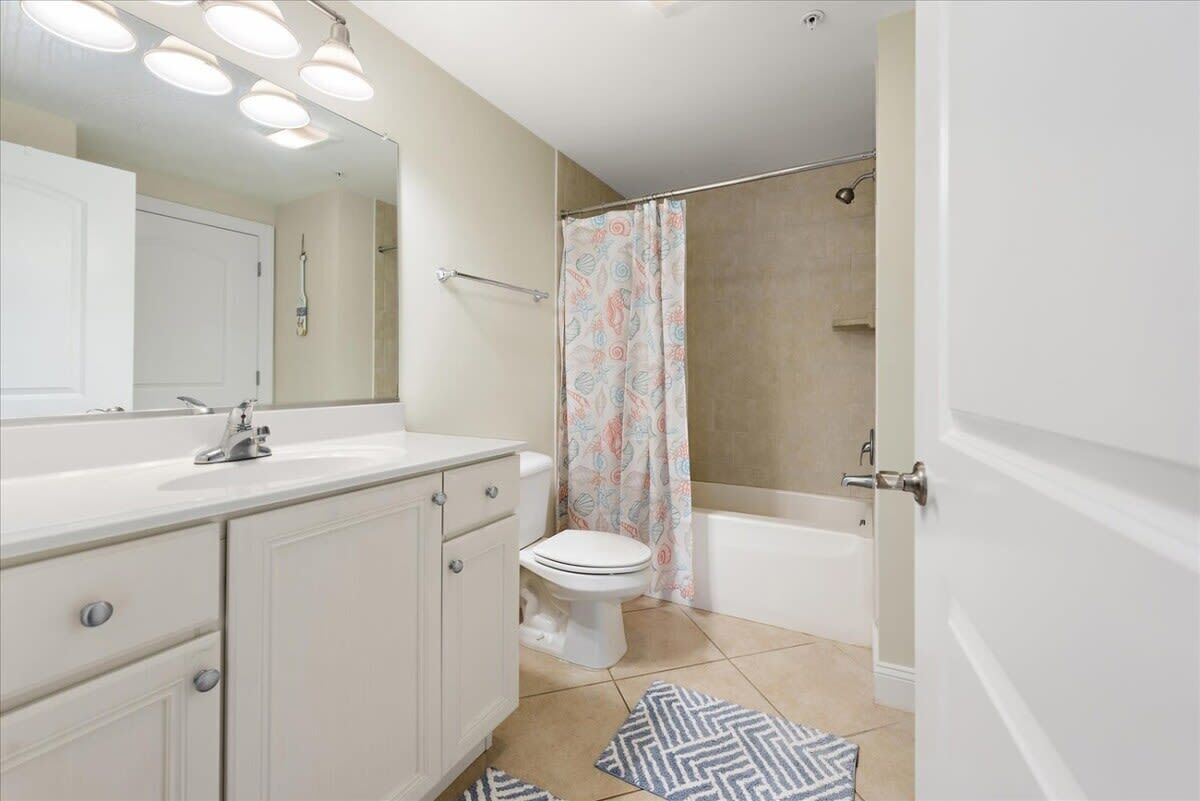 Une salle de bain équipée de toilettes, d’un lavabo, d’un miroir, d’un rideau de douche et d’une baignoire.