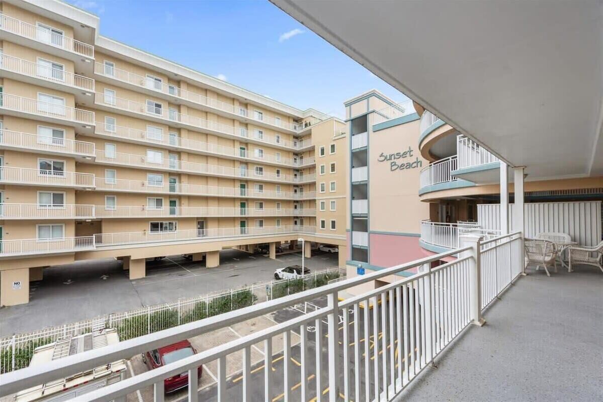 Un edificio de varios pisos con balcones, un estacionamiento y un letrero que dice 'Sunset Beach'.