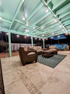 An outdoor patio area with a covered seating arrangement, including sofas and chairs, and a patterned rug on the floor. - Lower Foothills Light & Airy Mid-Century Charmer (Tucson)