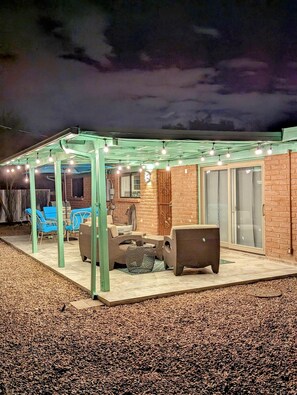 Un área de patio techada con asientos al aire libre, un muro de ladrillo y luces colgantes.
