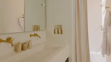Un baño con un lavamanos blanco, grifos dorados, un espejo y una toalla colgada en la pared.