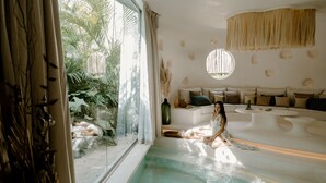 A spa-like room with a large window, a bathtub, and a sofa with cushions.