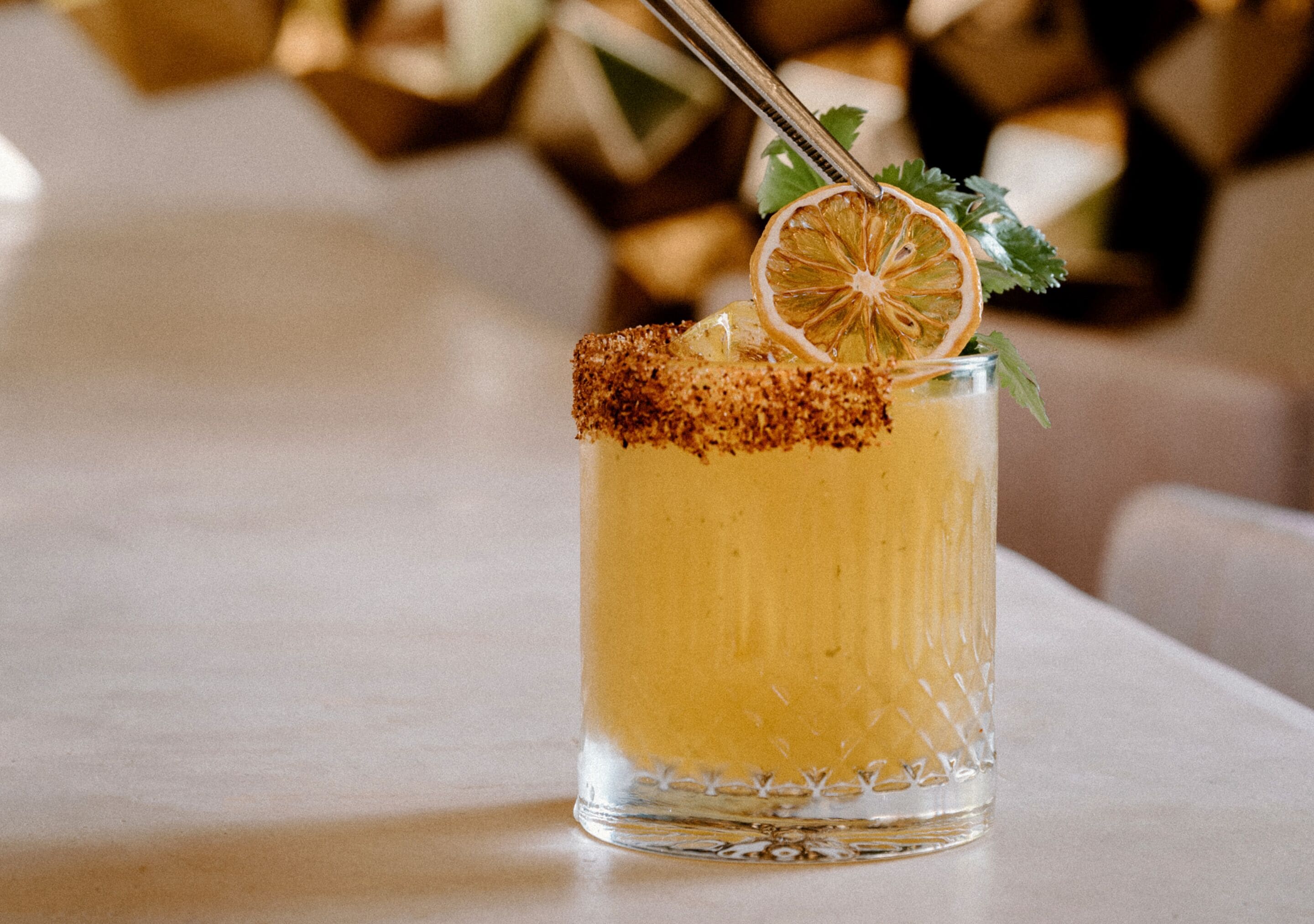 A cocktail glass with a salted rim and garnished with a slice of orange and a sprig of parsley.