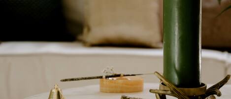 A green candle on a white table with a brass holder, a small bell, and a candle in a glass container.