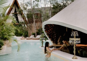 Un espace aménagé au bord de la piscine, comprenant un bar, des chaises longues et un coin salon abrité.