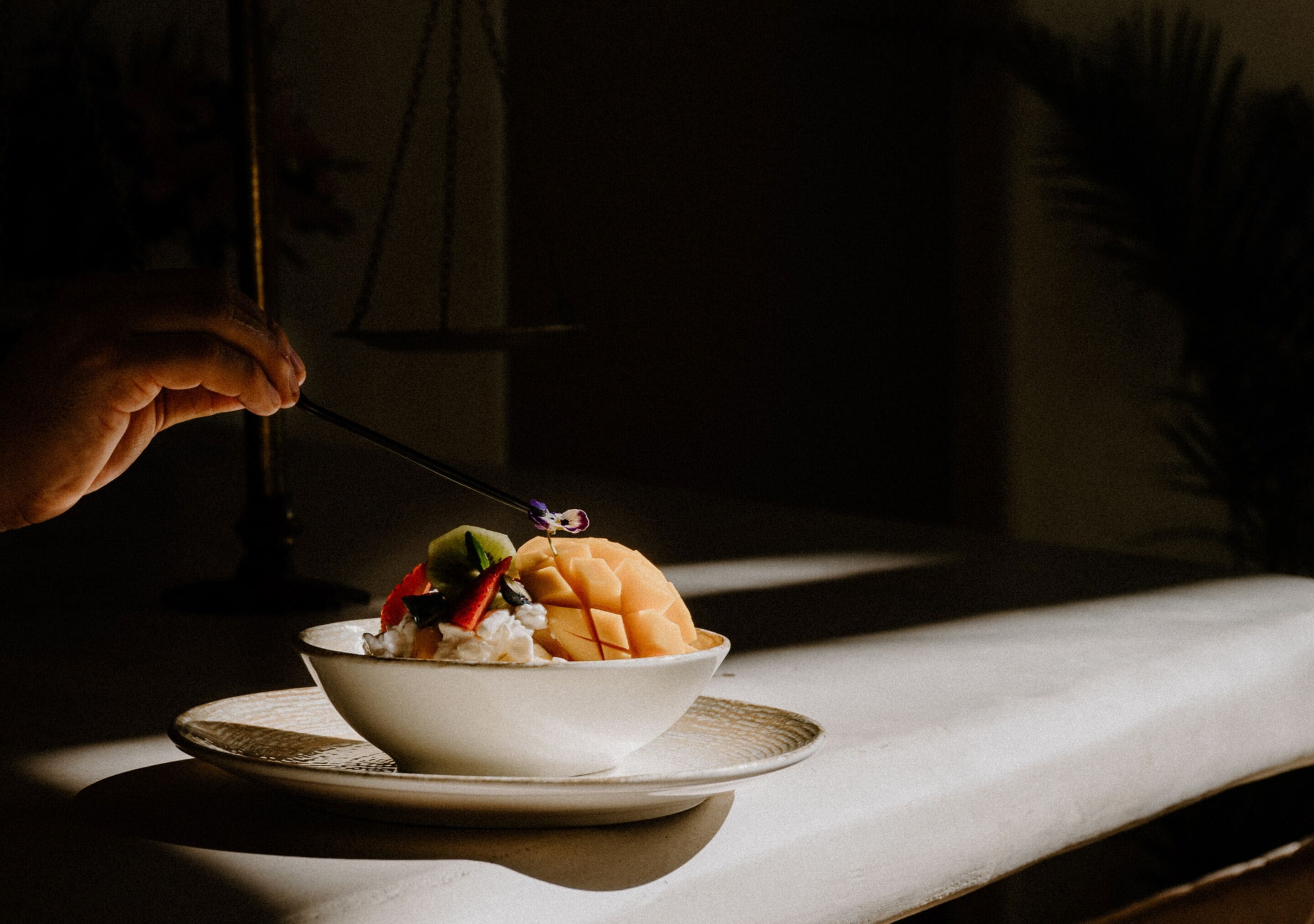 A bowl of food on a plate with a spoon, in a dimly lit room.