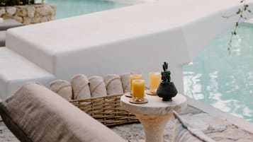 A poolside area with lounge chairs, a small table with drinks and bread, and a decorative figure.