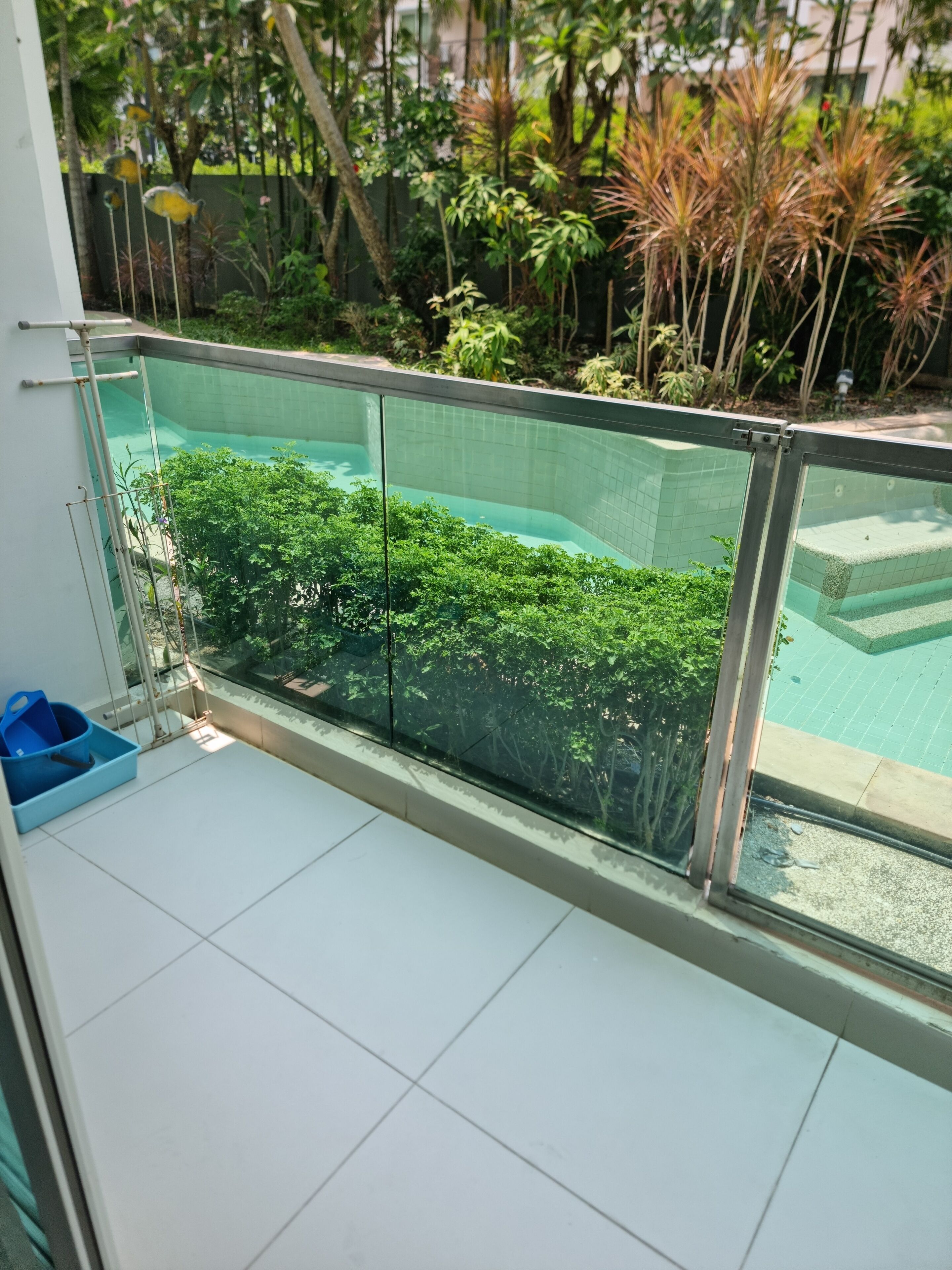 Un balcon doté d’une balustrade en verre, offrant une vue sur une piscine et une végétation luxuriante.
