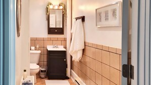 A narrow bathroom with a toilet, sink, and mirror. There are towels and toiletries on the floor. - Warm northwoods beach-style apartment walking distance to OreBeGone & Mesabi Trl (Gilbert)