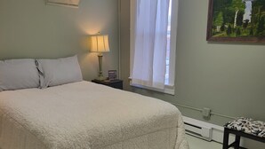 A bedroom with a large bed, a bedside table with a lamp, a window with sheer curtains, and a painting on the wall. - Warm northwoods beach-style apartment walking distance to OreBeGone & Mesabi Trl (Gilbert)