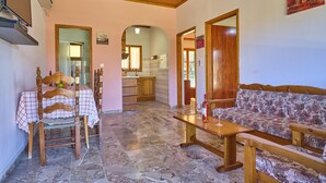 A living room with a wooden ceiling, a sofa, a table with a bottle and glass, and a chair with a tablecloth. - Theodora Apartment 2 Agios Stefanos Corfu (Corfu)