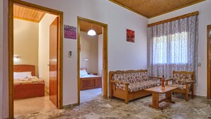 A room with a wooden ceiling, a stone-tiled floor, a sofa set, a small table, and a bed in the adjacent room. - Theodora Apartment 2 Agios Stefanos Corfu (Corfu)