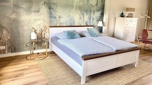 Un dormitorio con una cama grande, una mesita de noche con lámpara, un aparador y un armario.