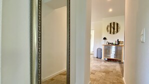 Un pasillo con un espejo grande y ornamentado, un reloj en la pared y una zona de cocina con un lavabo y armarios.