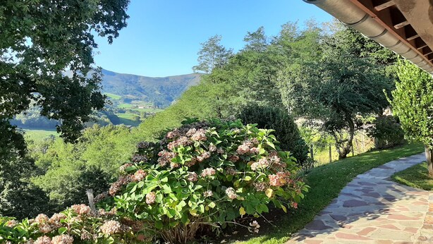 A stone pathway leading through a lush garden with a variety of shrubs and trees, overlooking a scenic valley. - Chalet Avec vue Magnifique sur les Montagnes Basques, à 3 Minutes Despelette (Itxassou)