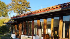 A house with a stone patio, wooden porch, and large windows. - Chalet Avec vue Magnifique sur les Montagnes Basques, à 3 Minutes Despelette (Itxassou)