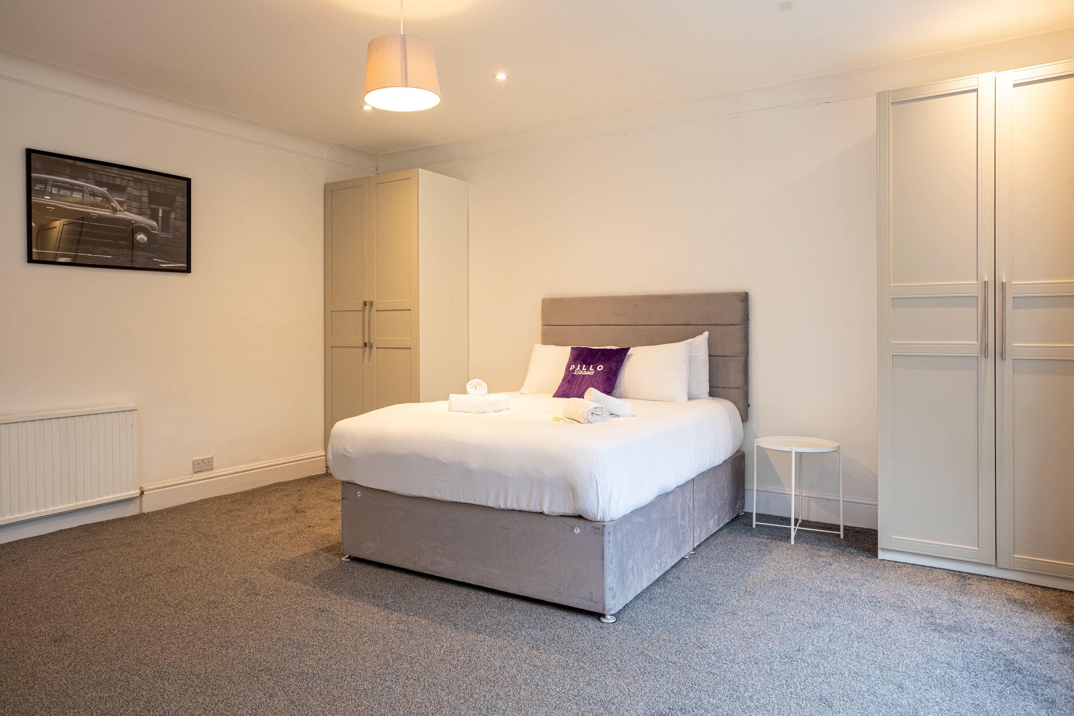 A neatly arranged bedroom with a bed, a side table, a wardrobe, and a hanging light fixture.