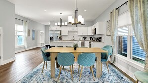 A modern kitchen with white cabinets, a central island, and a dining area with a wooden table and blue chairs. - Modern & Spacious Downtown Master Suite Palace! (Indianapolis)
