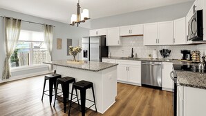 A modern kitchen with white cabinets, a granite countertop, and a central island with bar stools. - Modern & Spacious Downtown Master Suite Palace! (Indianapolis)