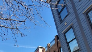 A row of multi-story buildings with commercial storefronts on the ground floor, a clear sky, and a sidewalk with a few parked cars. - Modern & Spacious Downtown Master Suite Palace! (Indianapolis)