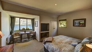 A bedroom with a bed, a desk with a chair, a television, and a window with curtains. - Hidden Lodge (Queenstown)