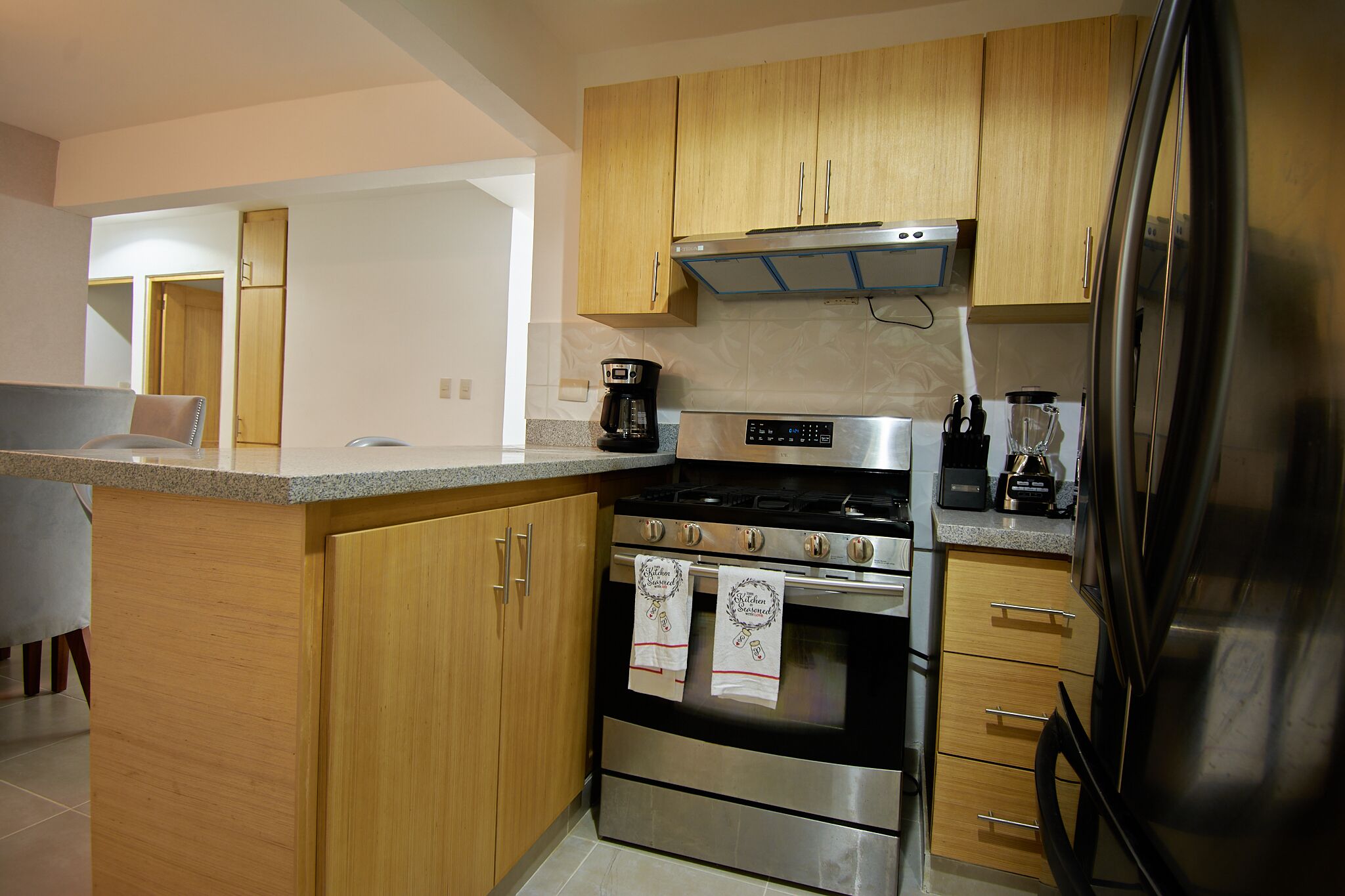 A modern kitchen with wooden cabinets, a stainless steel refrigerator, and a built-in oven.