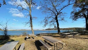 A lakeside picnic area with picnic tables and benches, surrounded by trees and a view of the lake.