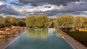 Piscina con sillas de descanso y vistas a árboles bajo un cielo nublado.