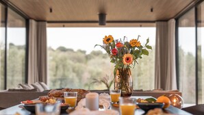 Una mesa de desayuno con diferentes platos, un jarrón de flores y vistas al exterior.