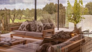Una sala moderna con un sofá, una mesa de centro y vistas a un jardín a través de amplios ventanales.