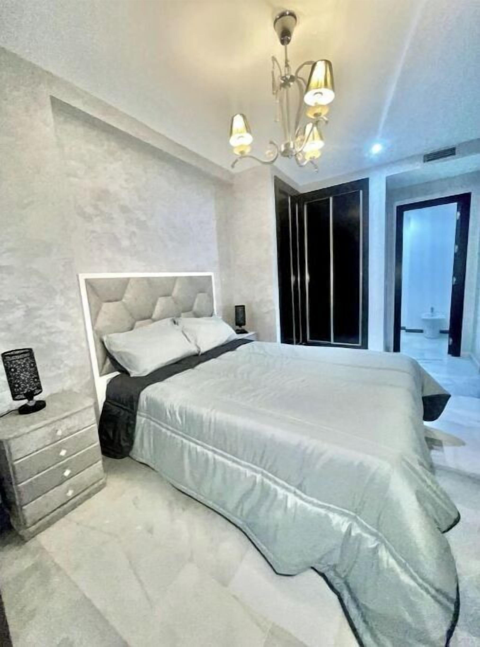 A modern bedroom with a large bed, a nightstand, a wall-mounted lamp, and a wardrobe.
