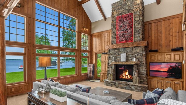 A spacious living room with large windows overlooking a lake, a stone fireplace, and a cozy seating area. - NEW! Sunsets Abound in Cross Lake Splendor (Crosslake)