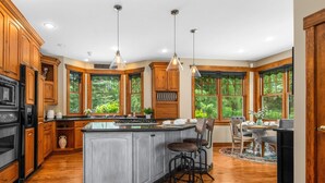 A spacious kitchen with wooden cabinets, a central island, and large windows offering a view of greenery. - NEW! Sunsets Abound in Cross Lake Splendor (Crosslake)