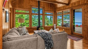 A cozy cabin interior with a wooden interior, large windows, a sofa, and a fireplace. - NEW! Sunsets Abound in Cross Lake Splendor (Crosslake)