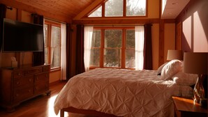 A bedroom with a large bed, wooden ceiling, and multiple windows.