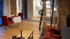 A spacious living area with a wooden ceiling, a dining table with chairs, a sofa with cushions, and a kitchen in the background. - Vacation cottage Schorenmoos-Lodge (Dietmannsried)