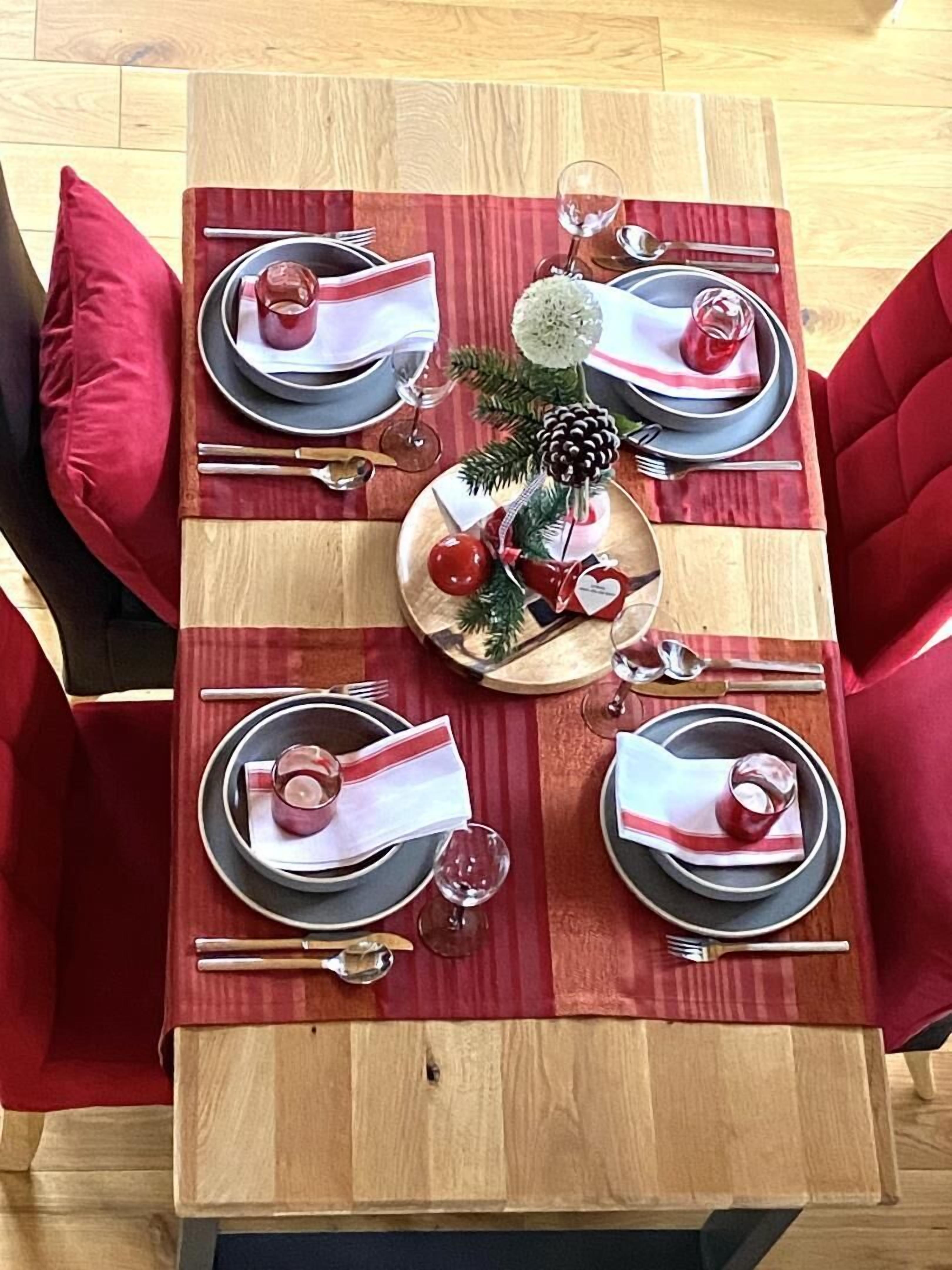 A dining table set for four with red upholstered chairs, a wooden centerpiece, and a striped table runner.