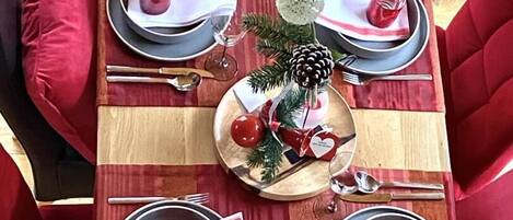 A dining table set for four with red upholstered chairs, a wooden centerpiece, and a striped table runner.
