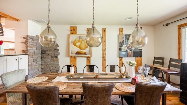 Uma sala de jantar com uma mesa de madeira, cadeiras e luminárias pendentes.