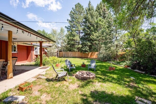 A backyard with a covered patio, outdoor seating, a fire pit, and a wooden fence. - Single level home (+basement) near Old Town & CSU (Fort Collins)