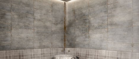 A modern, minimalist bathroom with a concrete wall and floor, a bench, a towel, and a pitcher.