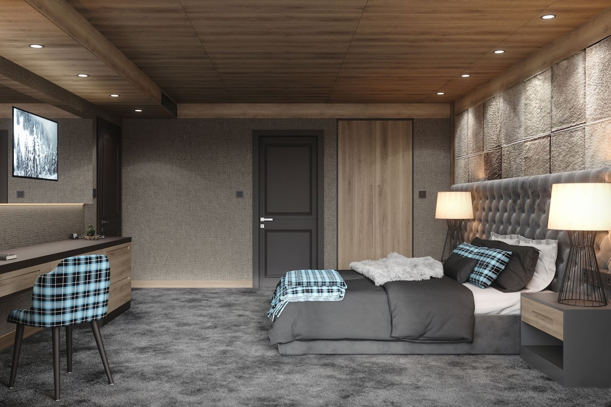 A modern bedroom with a desk, a bed with a tufted headboard, and a large wall-mounted TV.