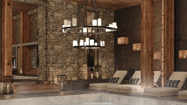 Un espace spa agrémenté d’un mur en pierre, de poutres en bois et d’un lustre central. On y trouve des fauteuils confortables avec des coussins, ainsi qu’un grand sol réfléchissant.