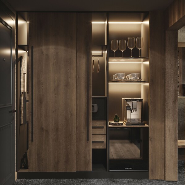 Un vestidor moderno y bien iluminado con puertas de madera, repisas con copas de vino, tazas y una cafetera.