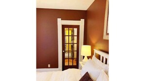 A hotel room with a bed, a nightstand with a lamp, and a door leading to a hallway.