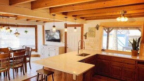 A kitchen with wooden beams, a large island, bar stools, and a TV mounted on the wall.