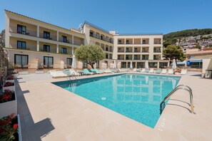A swimming pool with lounge chairs and umbrellas, a building with balconies, and a clear sky. - Hotel Coral Boutique by gaiarooms (Torroella de Montgrí)